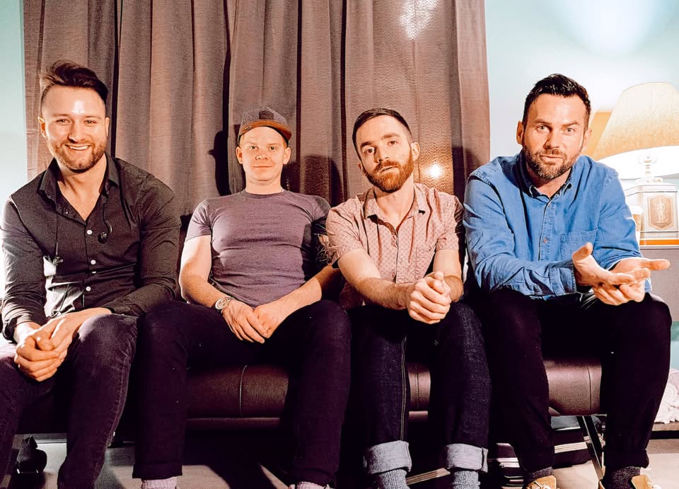 The four Windsor Drive members sitting together on a couch in front of curtains